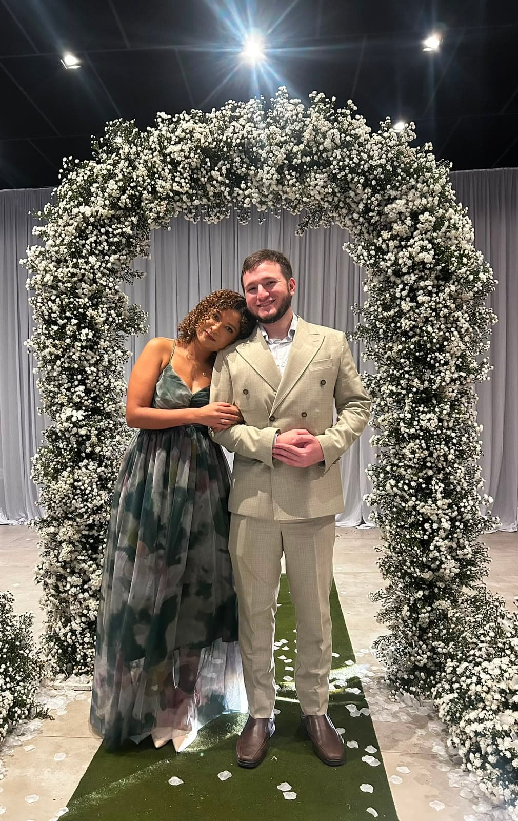 Jessyana e Pedro sorrindo sob o arco de flores