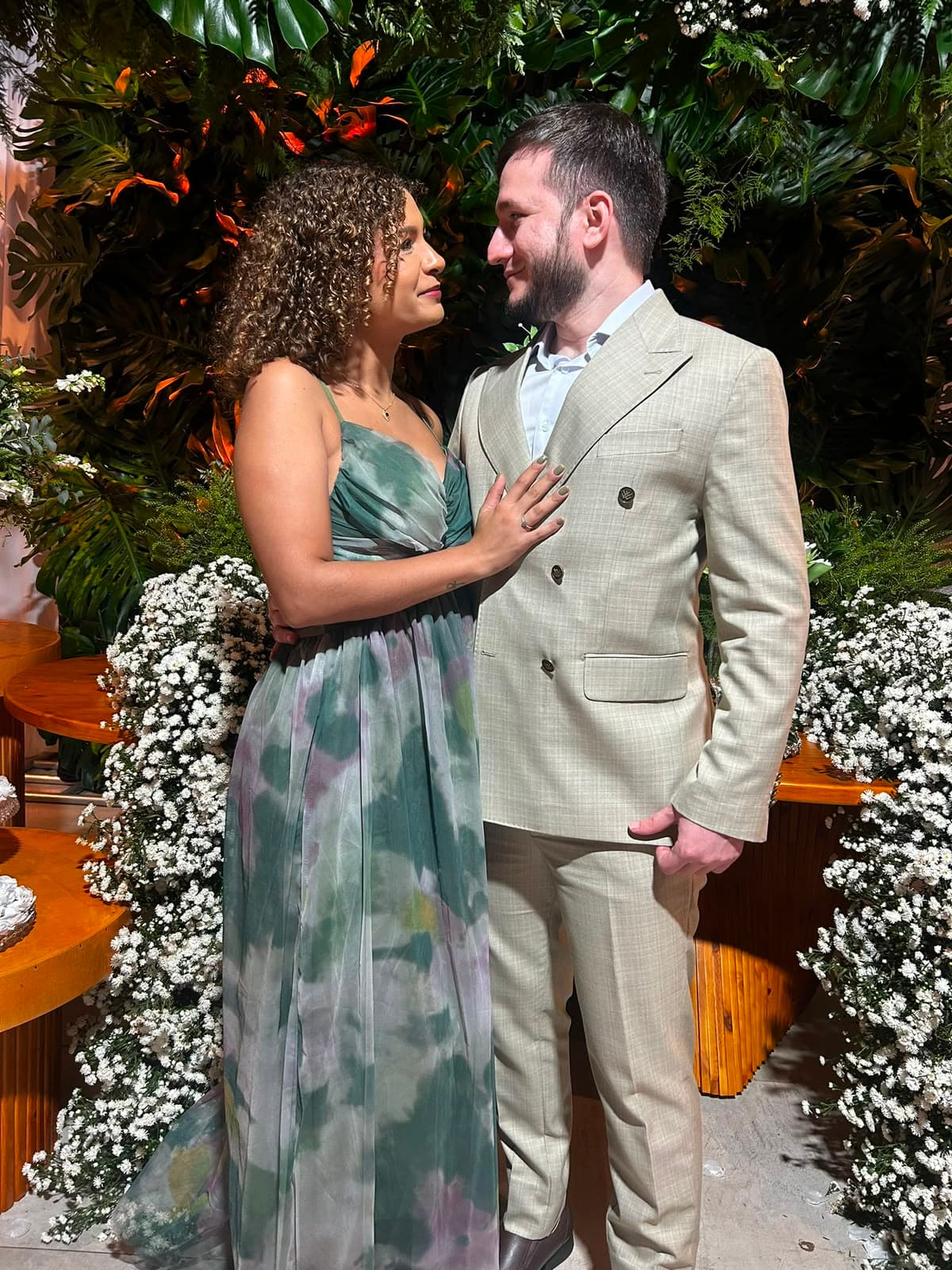 O casal se olhando em frente à decoração de folhagens