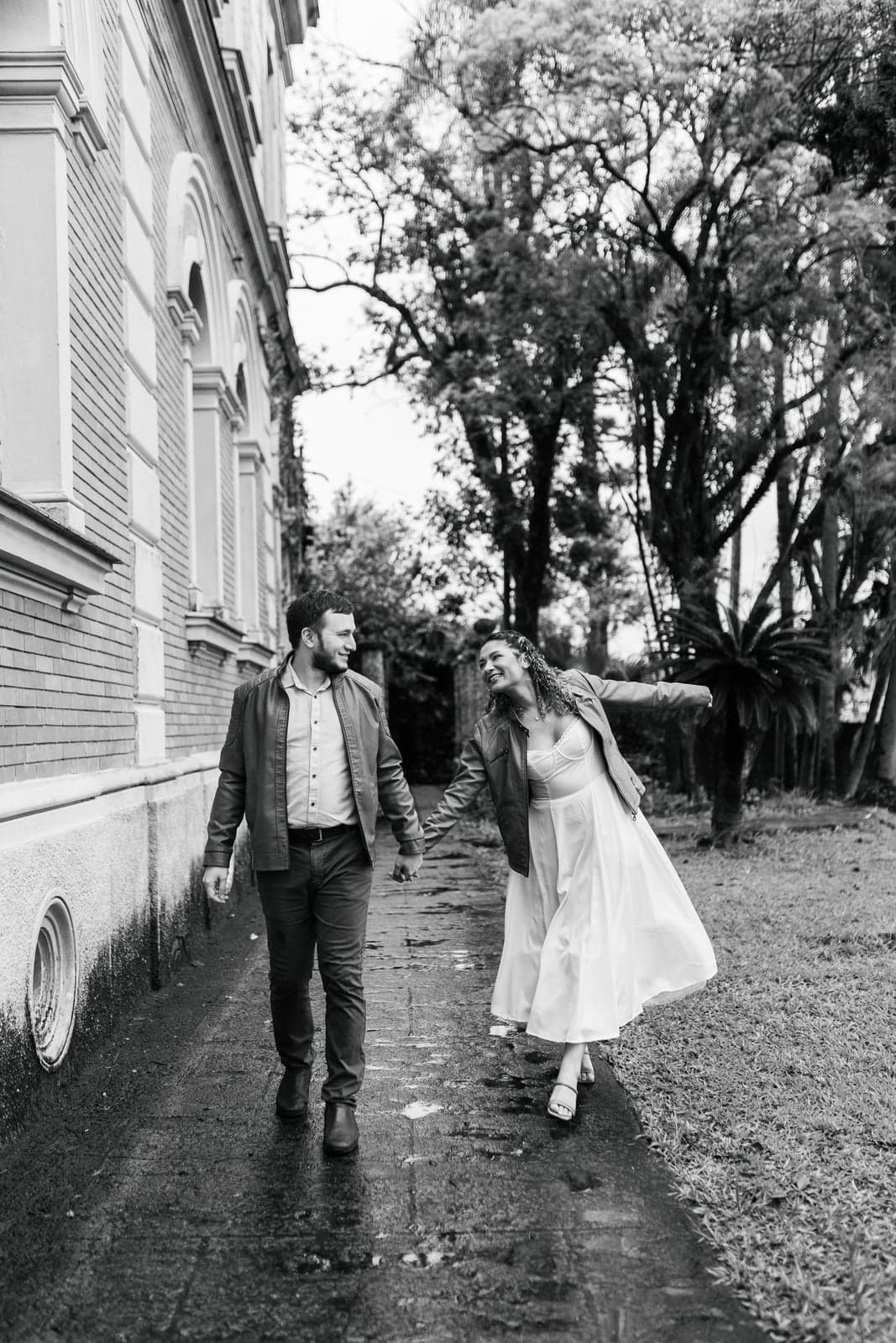 O casal caminhando de mãos dadas ao lado de um prédio antigo, foto em preto e branco