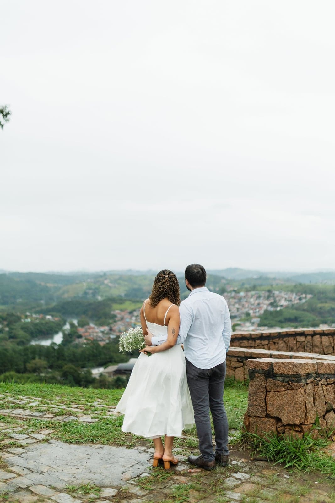 O casal abraçado de costas, admirando a vista da cidade do alto