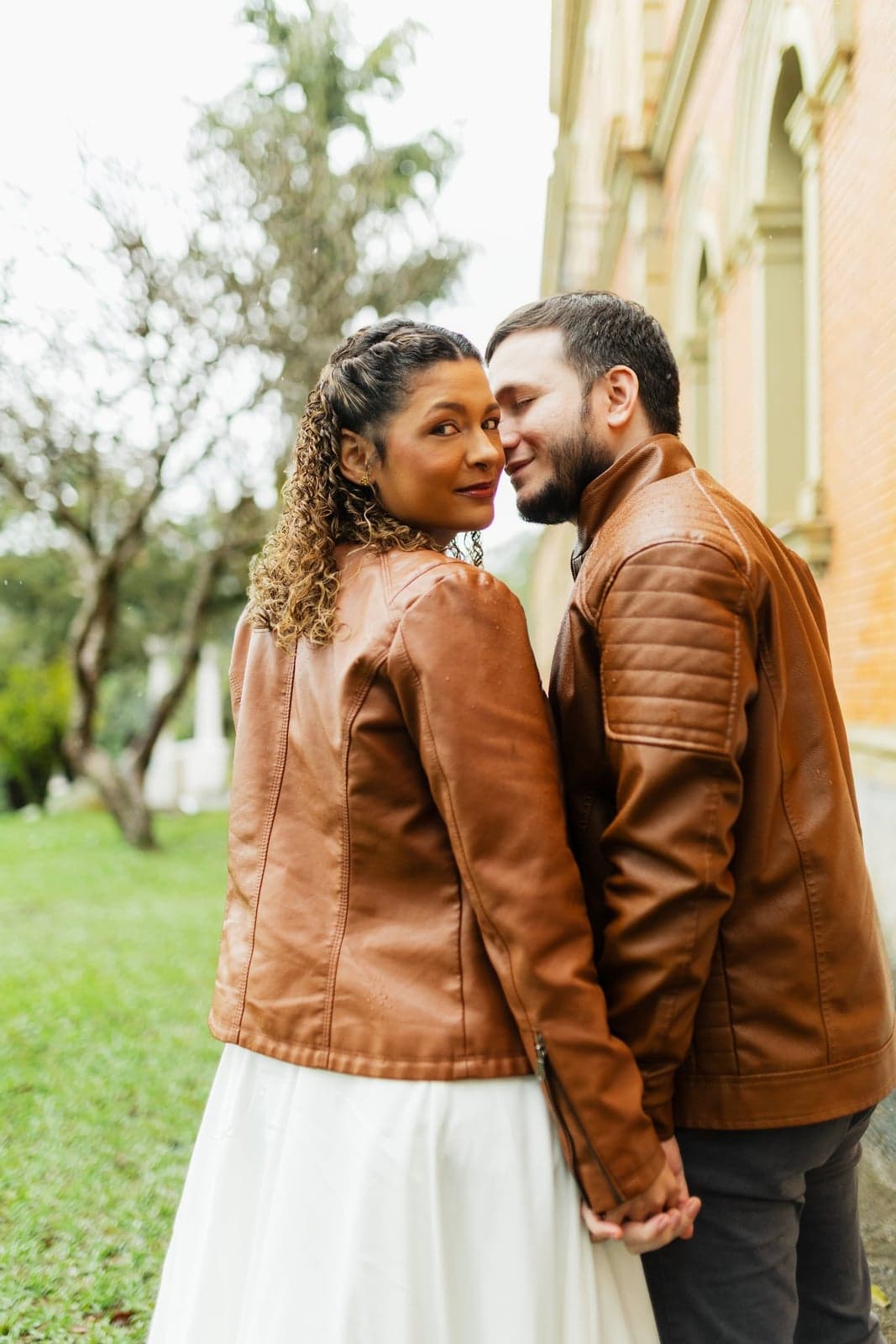 O casal se abraçando e sorrindo, Pedro de jaqueta de couro marrom